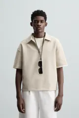 Polo color beige de corte relaxed fit, confeccionado en tejido interlock de algodón con elasticidad. Tiene cuello solapa con cierre frontal de cremallera y manga corta.