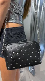 Bandolera negra con tachas plateadas, correa de cadena metálica y cierre superior.
