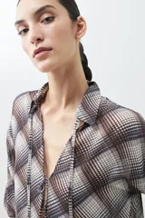 Camisa de manga larga con estampado escocés en tonos chocolate, blanco y gris. Presenta cuello camisero, cierre frontal con lazos y puños con lazos ajustables.