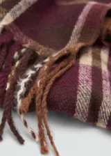 Bufanda rectangular con estampado de cuadros tartán en tonos marrón, beige, blanco y borgoña. Tiene flecos en los extremos.