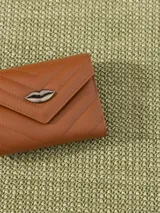 Billetera pequeña color visón, con solapa y cierre a presión. Diseño acolchado con pespuntes en forma de V y logo metálico con forma de labios.