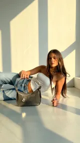 Cartera negra de cuero sintético con textura croco, para usar al hombro. Tiene hebillas metálicas para regular el largo de la correa, cierre YKK, dije metálico con el logo de la marca y forro interior.