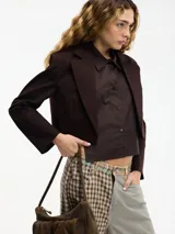 Blazer cropped marrón oscuro con solapa en la parte delantera y camisa desmontable mediante botones. Confeccionado en 97% algodón y 3% elastano.