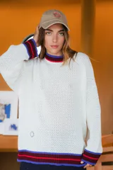 Sweater tejido de punto abierto color blanco, con cuello redondo y terminaciones en puños y ruedo a rayas en colores azul, rojo y bordó.