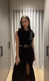Vestido midi negro sin mangas, con corte en la cintura y abertura frontal en la falda. Presenta un detalle de hebilla plateada en la cintura.