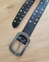 Cinturón negro de cuero con tachas plateadas y hebilla metálica rectangular con acabado envejecido.