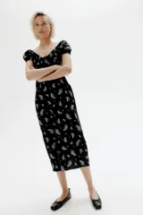 Vestido largo negro con estampado floral blanco, de tejido liviano de mezcla de lino y viscosa. Modelo con mangas cortas abullonadas, escote corazón con tiras finas y copas preformadas con frunces. Elástico fino en escote, hombros, mangas y cintura. Cierre lateral oculta y bajo recto con tajo pronunciado en un lado.