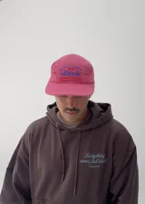 Gorro tipo gorra color fucsia con visera, y estampado frontal en azul con la palabra "attitude" y otros textos.