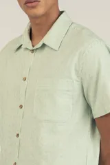 Camisa de manga corta celeste con rayas verticales blancas, cuello clásico, cierre frontal con botones y bolsillo de parche en el pecho.