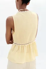 Blusa amarilla sin mangas con escote en pico y detalle de puntillas blancas. Cierre frontal con botones.