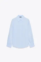 Camisa celeste de cuello solapa y manga larga con pliegues. Bajo asimétrico y cierre frontal con botones.