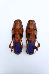 Sandalias de cuero color borgoña con textura croco, diseño cerrado en la parte delantera con aberturas laterales, punta cuadrada y cierre con hebilla ajustable en el tobillo. Taco ancho de 3 cm.