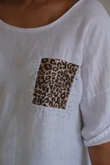 Blusa blanca de lino con cuello redondo y mangas 3/4 con botón. Tiene un bolsillo de parche con estampado animal print en el pecho.