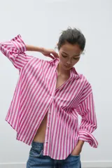 Camisa de popelín a rayas verticales rosas y blancas, de corte holgado, con cuello solapa, escote pico y mangas largas con puños abotonados.