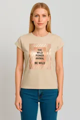 Remera color beige de corte clásico con mangas cortas. Presenta un estampado rectangular con bordes difuminados y texto en color cobre que dice "The Wild Power Animal Be Wild".