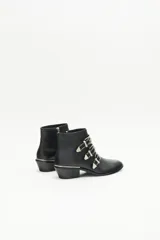 Bota de caña corta de cuero negro con tres tiras cruzadas decoradas con remaches, hebillas y puntera metálica. Tiene cierre lateral y taco ancho de 4 cm con vira metálica.
