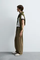 Pantalón color caqui de corte tapered relaxed fit, confeccionado en tejido de algodón. Presenta cintura con pliegues frontales dobles, bolsillos laterales en cadera y bolsillos traseros de vivo con botón. Cierre frontal con cremallera y botón.