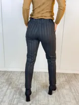 Pantalón negro con finas rayas verticales color beige, corte recto, cintura elástica con lazo y bolsillos laterales.