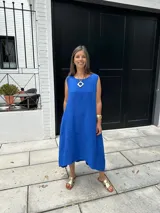 Vestido midi azul francia de lino, con escote redondo, sin mangas y bolsillos laterales. De corte acampanado y costuras que le aportan estructura.