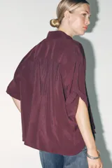 Camisa color borgoña de corte amplio, confeccionada en tejido fluido con modal. Tiene cuello solapa, manga corta con dobladillo y cierre frontal con botones.