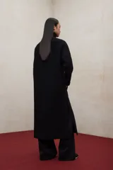 Abrigo largo de lana reciclada en color negro, con diseño minimalista, cuello redondo y cierre frontal con botones ocultos. Presenta aberturas laterales, bolsillos frontales tipo parche y mangas largas.