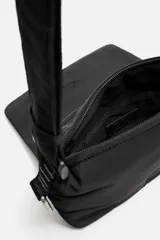 Bandolera negra de nylon con solapa y cierre magnético. Tiene correa ajustable con mosquetón y bolsillo interior.