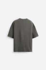 Camiseta color gris verdoso de punto tejido en hilatura de algodón, con cuello redondo, manga corta, efecto lavado y acabados irregulares.