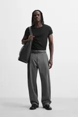 Pantalón gris de corte ancho con pliegues frontales y cinturón fino negro.
