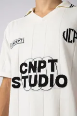 Remera tejida color crudo con cuello tipo chomba en V, mangas cortas con rayas negras y estampado con letras en el frente. Confeccionada en hilado de algodón.