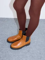 Bota Chelsea de cuero negro con estampado de cocodrilo, elástico lateral y suela de goma con pespuntes azules.