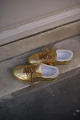 Championes deportivos de cuero y gamuza color dorado metalizado y marrón. Suela de caucho color crema con línea roja. Cordones color crema.