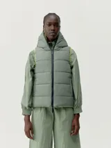 Chaleco gris acolchado con capucha y cierre frontal con cremallera blanca.