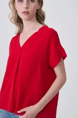 Blusa holgada de poliéster color blanco, con escote en V profundo y pinzas frontales que generan caída. Mangas cortas.