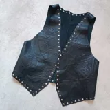 Chaleco sin mangas de cuero negro con detalles de tachas metálicas.
