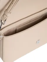 Cartera de hombro rectangular color beige claro, con solapa frontal y logo metálico de Calvin Klein. Incluye dos correas desmontables: una fina ajustable de cuero sintético y una ancha de tela tejida con el nombre de la marca repetido.