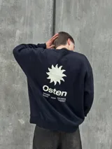 Buzo negro de corte holgado con cuello redondo y puños y bajo acanalados. Estampado frontal con un sol y la palabra "Osten" en blanco.