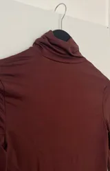 Top marrón de mangas largas con cuello alto y abertura en la cintura.