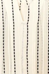 Blusa color crema con rayas verticales bordadas en negro. Tiene cuello redondo con escote en pico, mangas largas abullonadas y cierre frontal con botones.