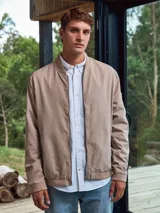 Campera bomber color beige, de Jack & Jones, con cuello de béisbol y cierre frontal con cremallera. Tiene bolsillos laterales con cremallera y un bolsillo en la manga.