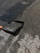 Gafas de sol negras con montura rectangular gruesa y lentes oscuras.