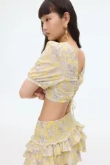 Blusa cropped de algodón color amarillo con estampado paisley en tonos grises. Tiene escote cuadrado elástico, mangas cortas con puños ajustados, espalda descubierta y tiras para atar.