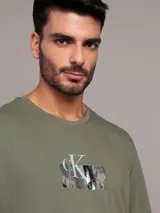 Remera verde militar de algodón, con cuello redondo y logo de Calvin Klein estampado en el pecho dentro de un recuadro blanco.