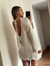 Vestido corto tejido en algodón y lurex color crudo, con punto pavo real, manga larga y escote en la espalda.