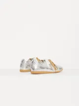 Zapatilla plateada de cuero vacuno con recortes en cuero descarne, doble cordón (uno blanco y otro marrón con pintitas) y charms colgantes.