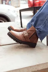 Bota corta color marrón de cuero, con hebilla metálica y cierre lateral.
