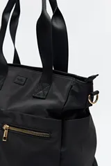 Bolso tote marrón de nylon con doble asa de mano negra y correa bandolera negra regulable y desmontable. Tiene dos bolsillos frontales con cierre metálico dorado.