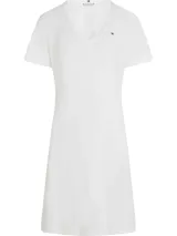 Vestido blanco de algodón regenerativo, corte recto y holgado, con cuello en V y manga corta. Presenta un pequeño logo bordado de Tommy Hilfiger en el pecho.