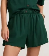 Short blanco de corte runner evasé, con cintura elástica fruncida y un botón decorativo. Presenta bolsillos laterales y un calce suelto.