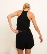 Conjunto de pijama corto negro confeccionado en Rib sin estampa. Incluye blusa con breteles finos, escote nadador en la espalda y aplicación de lazos; y short con cintura elástica y bajo frufru.
