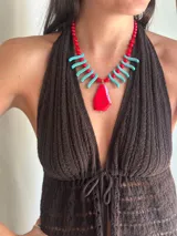 Collar de cuentas con dije central grande de piedra roja irregular, flanqueado por bastones turquesa y cuentas rojas redondas. La cadena es de eslabones finos con cierre regulable.